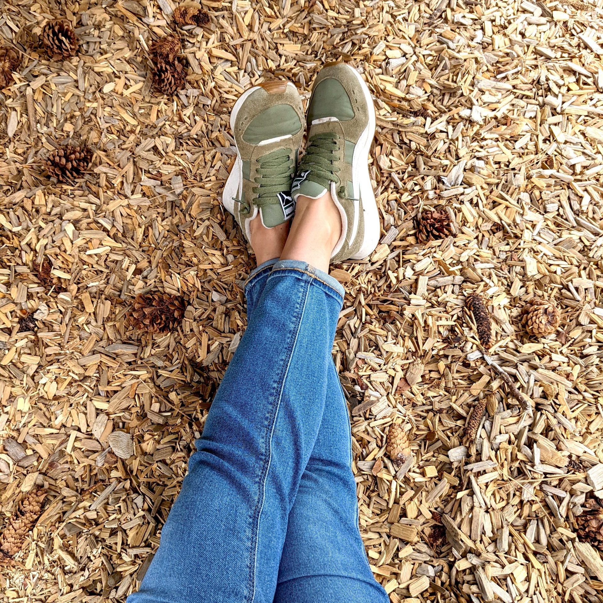 legs extended with feet crossed sitting in wood chips with pine cones